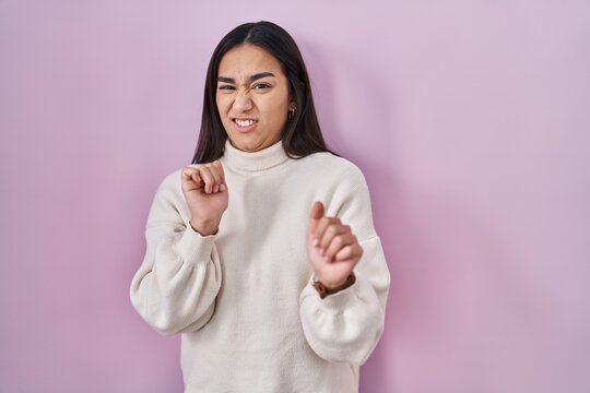 Young south asian woman standing over pink background disgusted expression, displeased and fearful doing disgust face because aversion reaction.