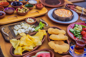 Turkish breakfast table. Pastries, vegetables, greens, olives, cheeses, fried eggs, spices, jams, honey, tea in copper pot and tulip glasses, wide composition