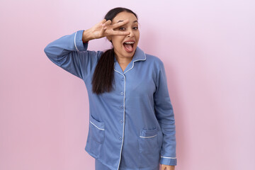 Young arab woman wearing blue pajama doing peace symbol with fingers over face, smiling cheerful showing victory