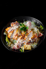 Caesar salad with croutons, cheese, eggs, tomatoes and grilled chicken on black wooden table