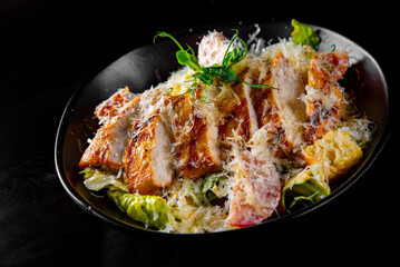 Caesar salad with croutons, cheese, eggs, tomatoes and grilled chicken on black wooden table
