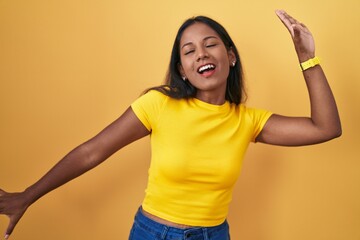 Young indian woman standing over yellow background dancing happy and cheerful, smiling moving casual and confident listening to music