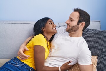 Man and woman interracial couple hugging each other lying on sofa at home