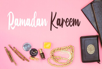 happy ramadan in english,  rosary, siwak and perfume and holy quran book with Arabic calligraphy meaning of Al Quran on pink background