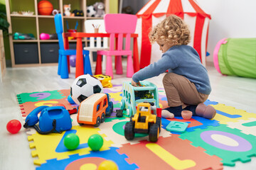 Adorable blond toddler playing with cars toy sitting on floor at kindergarten