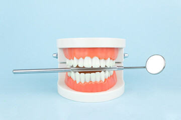 Dental prosthesis with dentist mouth mirror on blue background, close-up. Old age. Teeth. Jaw.