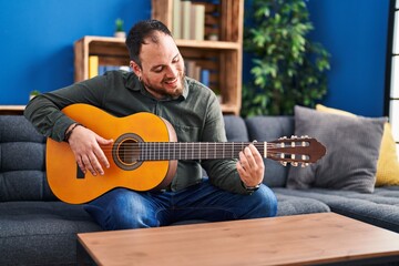 Obraz premium Young hispanic man playing classical guitar sitting on bed at home
