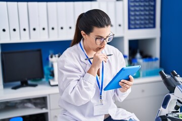 Young hispanic woman scientist using touchpad working at laboratory