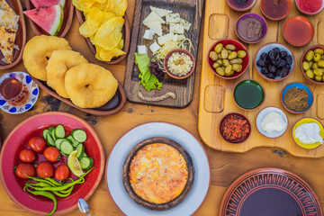 Turkish breakfast table. Pastries, vegetables, greens, olives, cheeses, fried eggs, spices, jams, honey, tea in copper pot and tulip glasses, wide composition