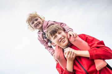 A little girl on her older brother's shoulders. Happy children on a walk. The teenage guy smiles sincerely. A teenager has braces on his teeth