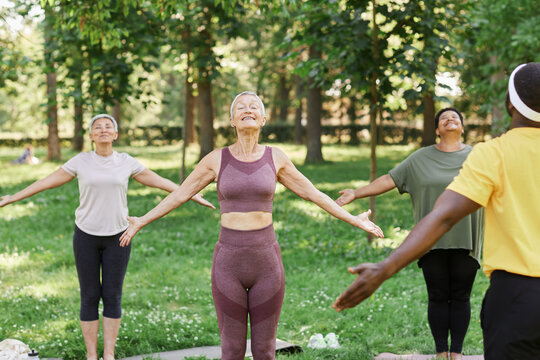 Group of active senior women enjoying yoga outdoors in park and doing breathing exercises