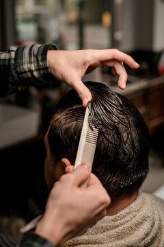 Close-up view of barber hands accurate combs wet male hair and make new style for client.