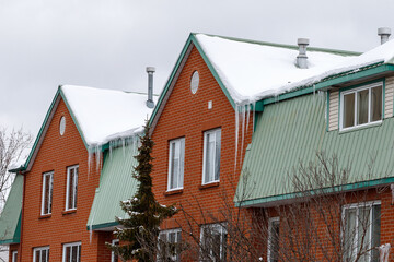 Residential building in winter. Icicles hanging from roofs of the houses covered with snow.
