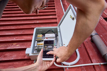 Consumer takes photo of readings of electricity meter in outdoor electrical panel using cell phone.