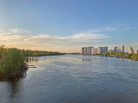 View of the deep river with the buildings in the background. Beautiful panoramic view of the city of Kyiv Dneper River at sunset on dark blue water with glowing reflected rays of the sun, copy-space