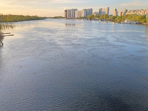 View of the deep river with the buildings in the background. Beautiful panoramic view of the city of Kyiv Dneper River at sunset on dark blue water with glowing reflected rays of the sun, copy-space