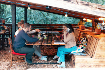 group of young people freelancer digital nomads sitting in cafe with tablet and laptop and cell phones while drinking juicy juices