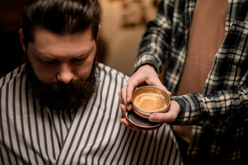 barber holds round jar of hair styling gel near the head of male client.