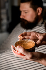 Selective focus on jar with hair gel for styling in male hands.