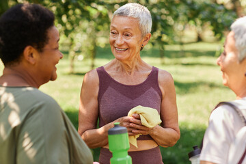 Waist up portrait of smiling senior woman chatting with friends after outdoor workout in park