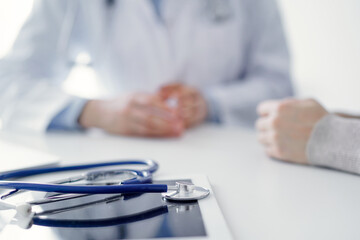 Stethoscope lying on the tablet computer in front of a doctor and patient at the background . Medicine, healthcare, reasuring hands concept