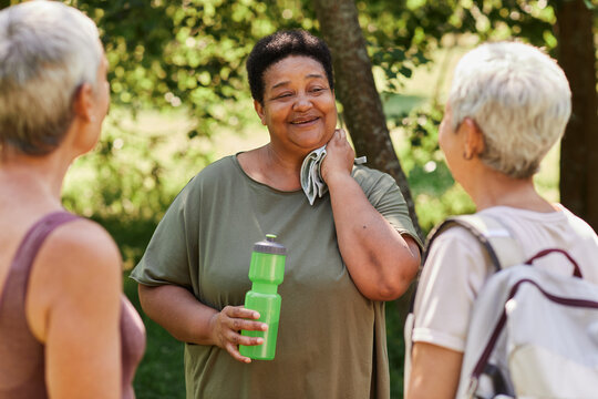 Waist up portrait of overweight senior woman chatting with friends after outdoor workout in park and smiling happily