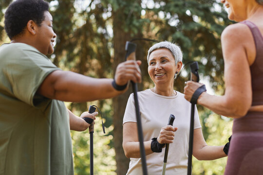 Waist up portrait of smiling senior woman with group of friends walking with poles together