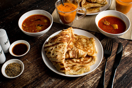 Malaysian Cuisine Roti Canai - Crispy Indian style pancake served with curry chicken dipping sauce with Thai ice tea on wooden table.