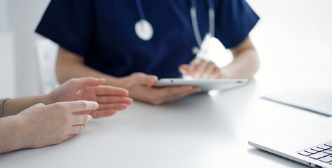 Doctor and patient talking to each other during current health examination while sitting at the desk in clinic, closeup of hand. Perfect medical service and medicine concept