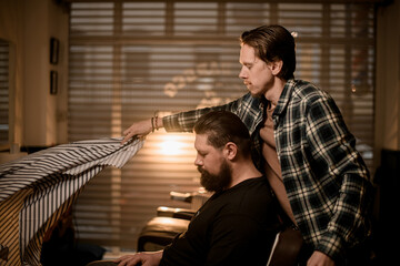 side view of bearded male client and barber gently putting hairdresser cape