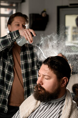 Male barber gently splashes water from the spray bottle at the head hair of his client