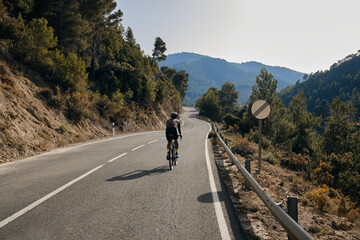 A professional cyclist riding a gravel bike on the empty road overlooking on mountains in Spain.