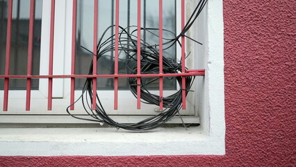Electric wires mess on residential window with metal bars. Visual city pollution