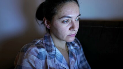 Fototapeta premium Casual woman in front of computer screen at night browsing internet using trackpad. Female person wearing pajamas in front of laptop seated at sofa at home