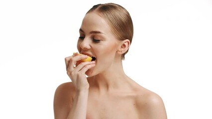 A blonde eats a fresh lemon on a white background