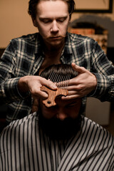 front view of barber doing hair styling to man with comb with long metal teeth