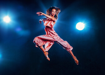 Young woman in pink dress jumping up on black background with lights