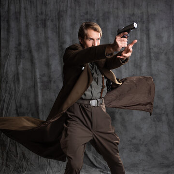 hero in a military style with a gun in his hands, a young man in a long brown coat and breeches with suspenders. he shoots a pistol in a spectacular pose, his coat flutters behind his back