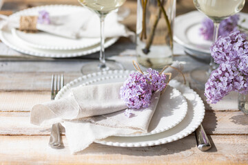 Beautiful table decor for a wedding dinner with a spring blooming lilac flowers. Celebration of a special holiday marriage event. Fancy white plates, wineglasses. Countryside style