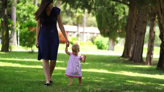 Little girl walks in the park by the hand with her mother and babbles