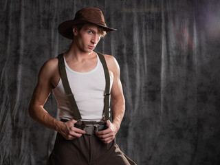 young man in a rural retro style, a character in an adventure western. A guy in a hat and a T-shirt, breeches with suspenders.