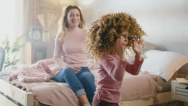 A little curly girl with a wig on her head is having fun and dancing around the room