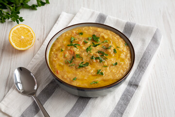 Homemade Lentil Soup with Parsley in a Bowl on a white wooden background, side view.