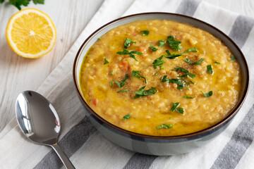 Homemade Lentil Soup with Parsley in a Bowl on a white wooden background, side view.