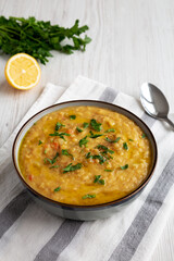 Homemade Lentil Soup with Parsley in a Bowl on a white wooden background, side view.
