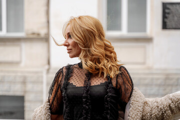 The blonde stands under a transparent umbrella during the rain. The fall season. Rear view. The woman is dressed in a black lace dress, her hair pulled back in a ponytail.