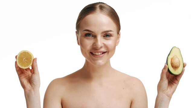 A beautiful young blonde girl holds half an avocado and half a lemon in her hands. Isolated on white background. The concept of health, body care, nutrition