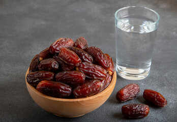 Glass of water with a bowl of date fruit on black background