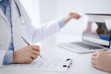 Fototapeta premium Doctor and patient discussing something and using laptop while sitting opposite each other at the desk in clinic office. Perfect medical service and medicine concept