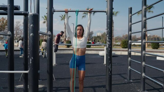 Slim young woman training pull ups with resistance band in outdoors at sunny summer day. Be H3althy